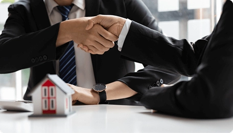 Dos personas cierran un acuerdo de inversión inmobiliaria con una maqueta de casa sobre la mesa